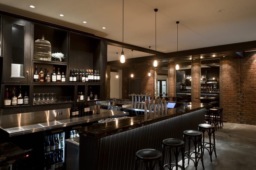 A contemporary black-stained timber bar and bottle display with polished concrete floor and exposed feature brickwork