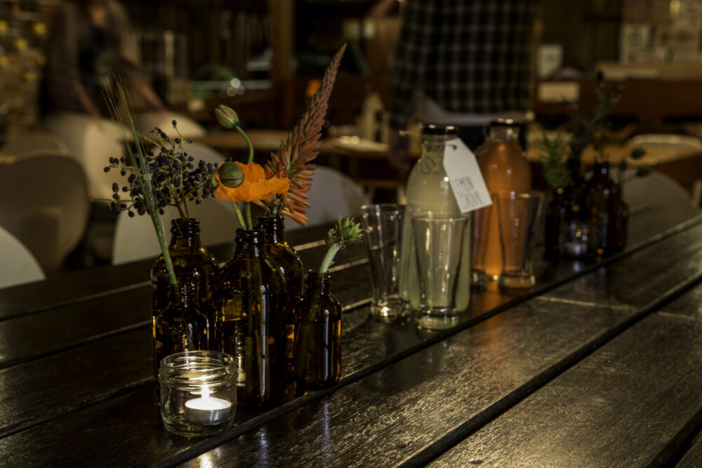 Amber bottles displaying winter florals, berries and grasses on timber tables with candles and bottles of home-made cordial